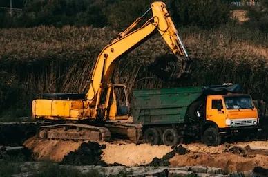 A tracked excavator loading soil with its bucket straight into a tipper body beside the dig