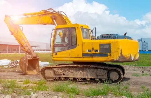A yellow tracked excavator with its bucket lowered on a plot of dug soil